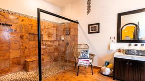 A bathroom with a glass shower enclosure, a wicker chair, a vanity with a mirror, and a patterned floor. - 1BR Studio w/balcony in Punta Sur (Isla Mujeres)