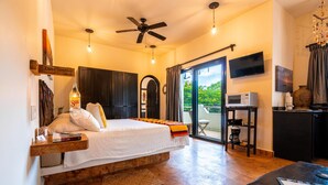 A spacious bedroom with a large bed, a ceiling fan, a TV, and a view of the outdoors. - 1BR Studio w/balcony in Punta Sur (Isla Mujeres)