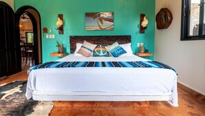 A bed with a striped blue and white bedspread, a white headboard, and pillows with the text "Happy Place." - 2BR Suite in Punta Sur w/Pool (Isla Mujeres)