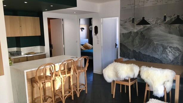 Una cocina moderna con armarios de madera, encimera blanca y un comedor con sillas de madera y una alfombra blanca mullida.