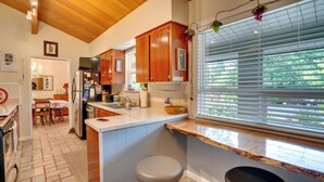 Une cuisine avec des meubles en bois, un plan de travail blanc et une fenêtre avec des stores.