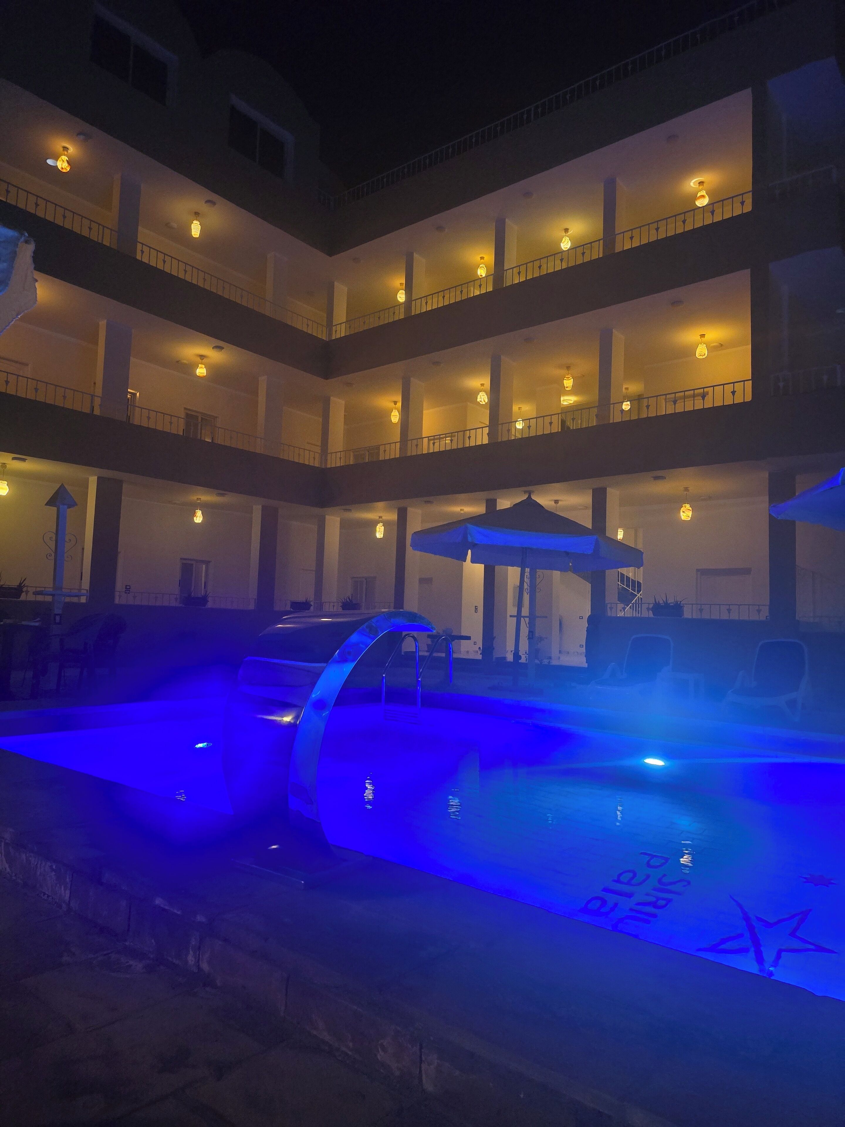 Een hotel met meerdere verdiepingen en een zwembadgedeelte verlicht met blauw licht.