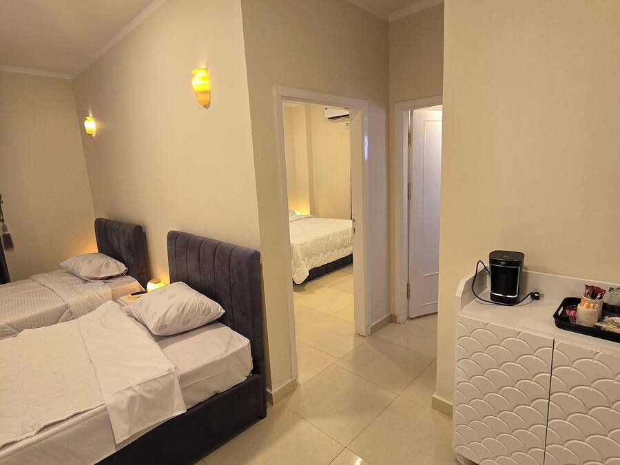 Una habitación de hotel con dos camas, una kitchenette pequeña y un baño visible a través de una puerta abierta.