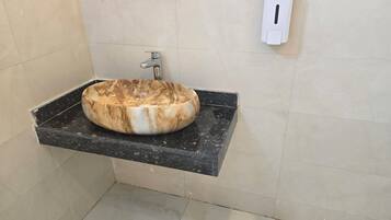 Une salle de bain avec un lavabo en marbre, un robinet, un distributeur de savon et une étagère en verre au-dessus du lavabo.
