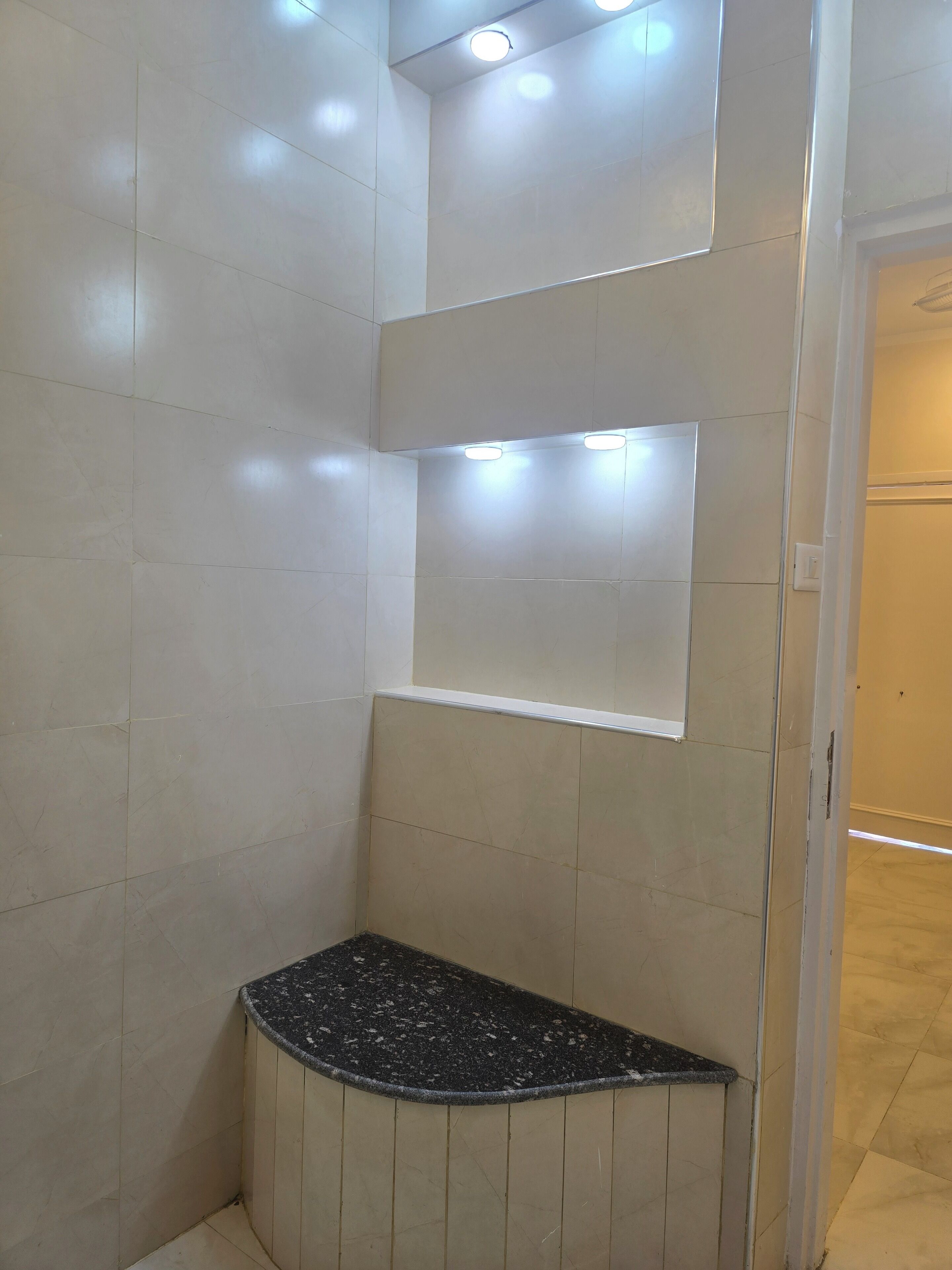 A bathroom with white tiled walls, a black speckled bench, and recessed lighting.