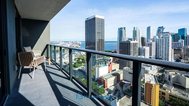 A balcony with a view of a cityscape, including high-rise buildings and a body of water. - New Luxury Condo in Downtown (Miami)