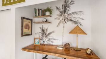 Un espacio de trabajo con un escritorio de madera, un cuadro enmarcado, un reloj, libros y un cuadro mural con motivos de palmera.