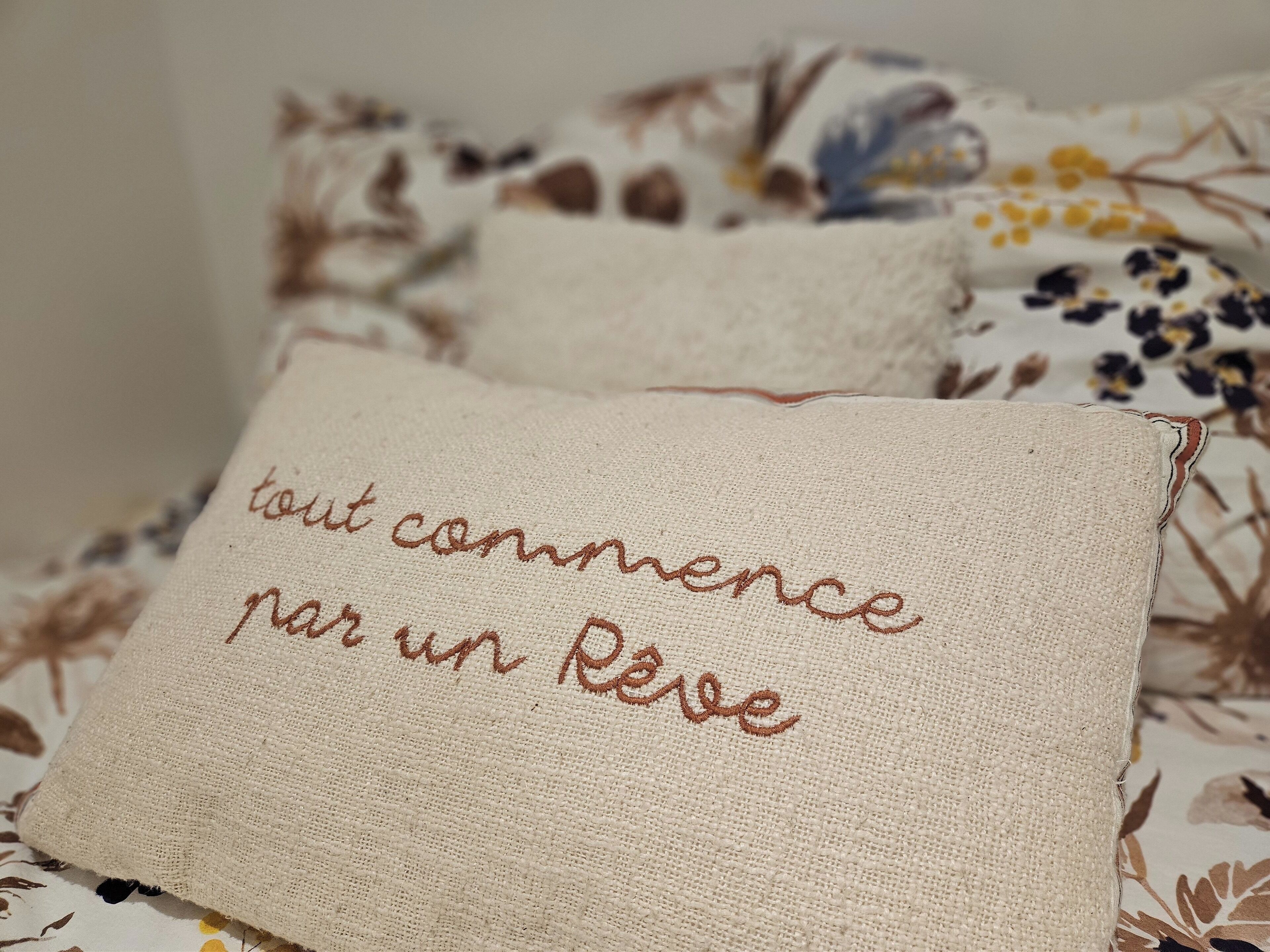Ein Bett mit einem blumigen Überwurf und einem Kissen mit aufgesticktem Text.