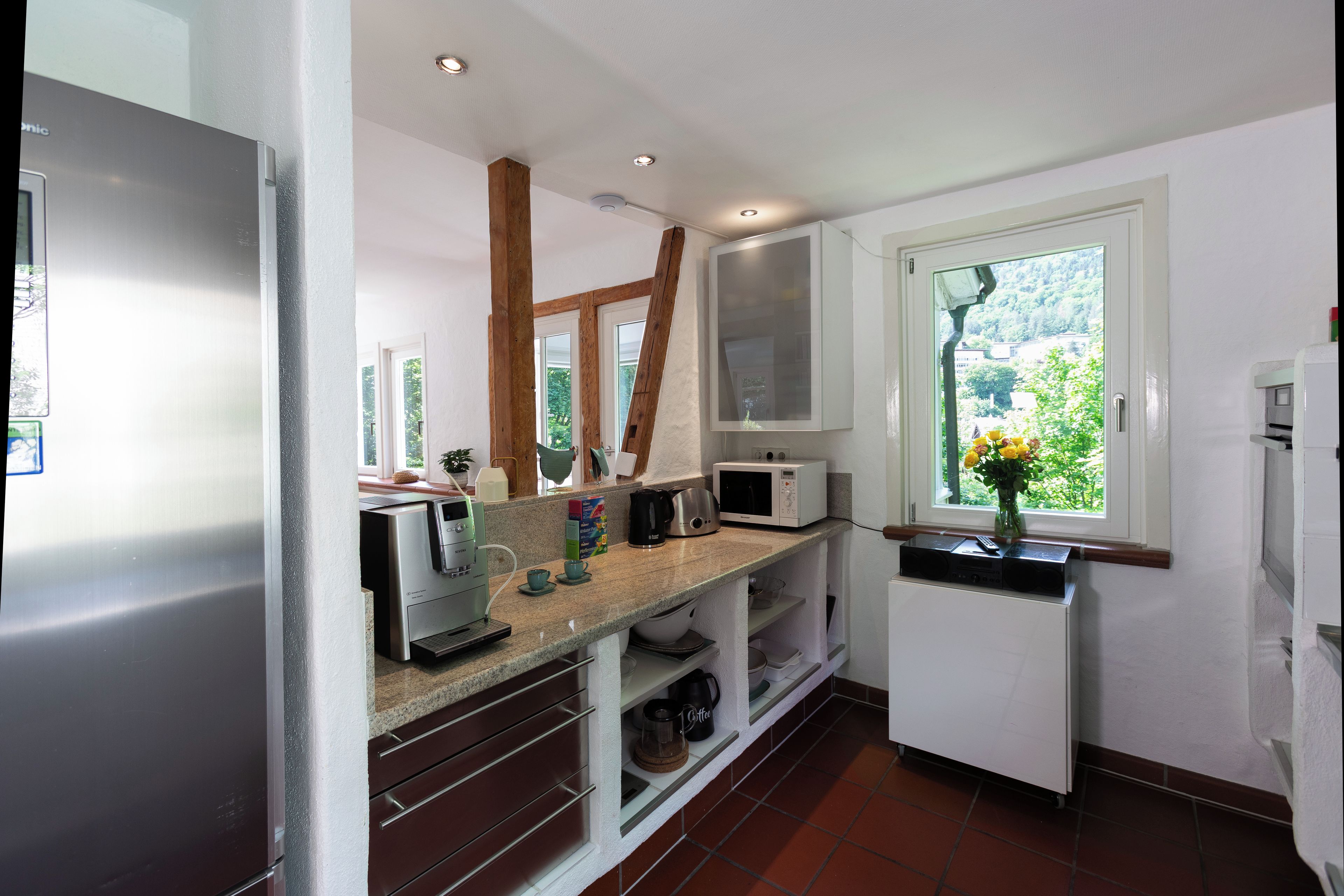 A modern kitchen with white cabinets, a built-in microwave, and a window with a view of greenery.