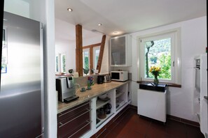 Une cuisine moderne avec des meubles blancs, un four à micro-ondes encastré et une fenêtre donnant sur un espace verdoyant.