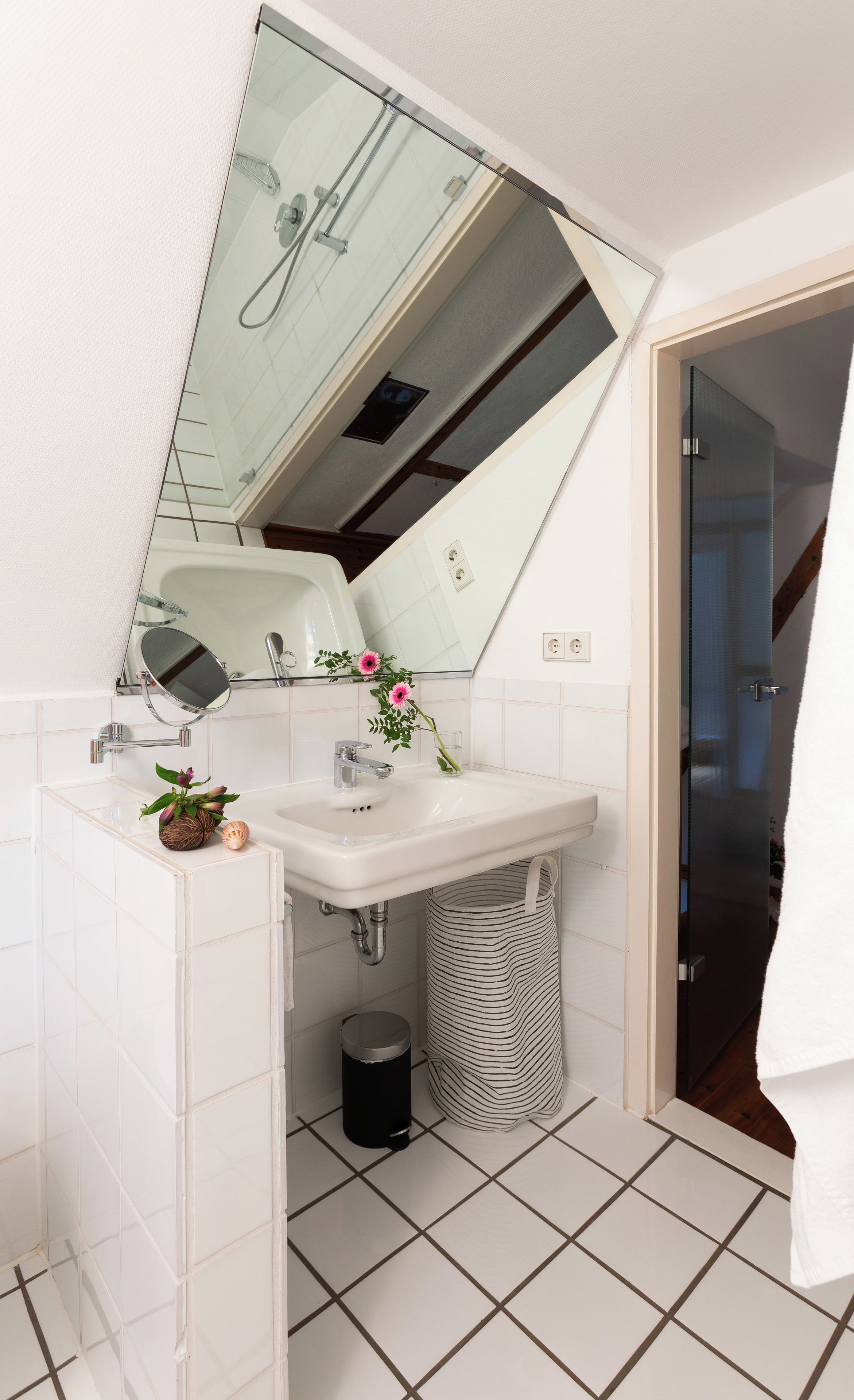 A modern bathroom with a white sink, a mirror, and a shower visible in the reflection.