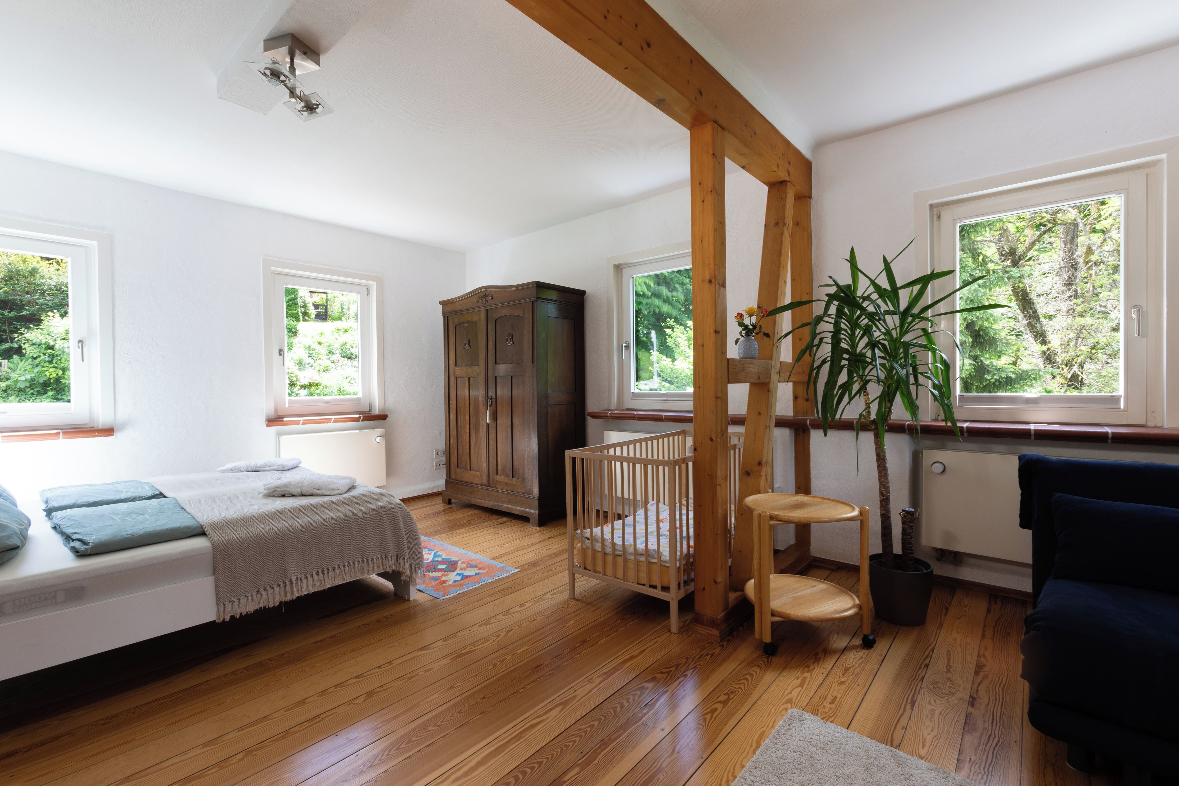 Une pièce comprenant un lit, un berceau en bois, une armoire et une plante en pot.