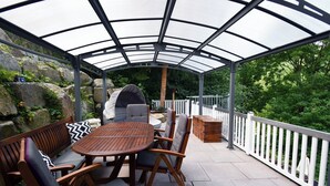 Un portico coperto con un tavolo rotondo in legno e sedie, un barbecue e una ringhiera bianca.