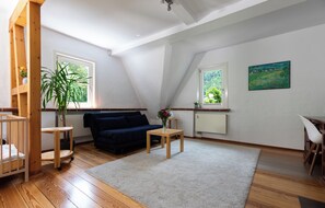 Un salon spacieux avec un canapé bleu foncé, des meubles en bois et de grandes fenêtres donnant sur un paysage verdoyant.