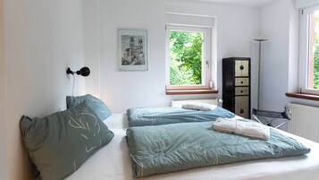 A bedroom with two beds, a window with a view of greenery, a radiator, and a cabinet.
