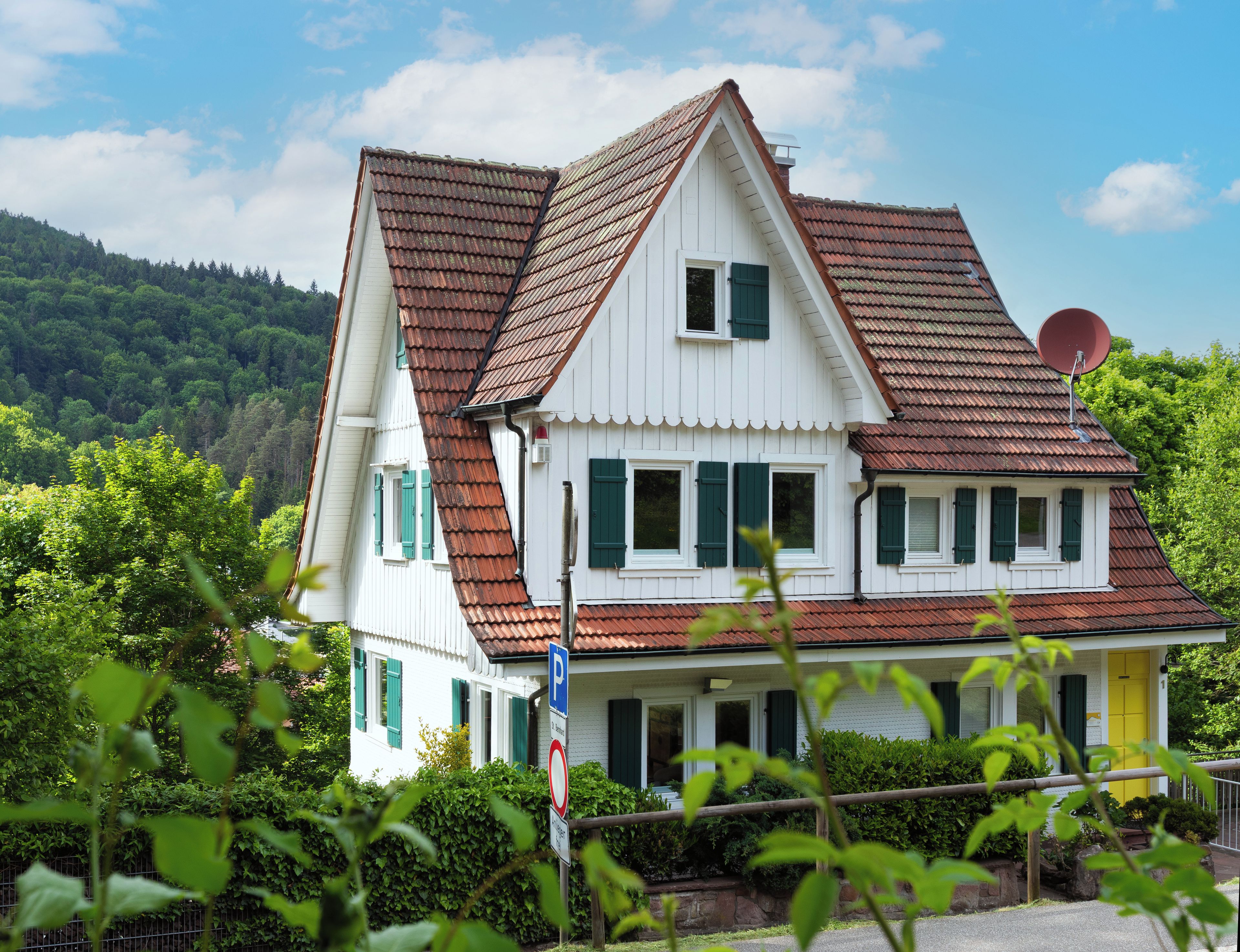 A two-story house with a steeply pitched roof, white exterior, and green shutters.