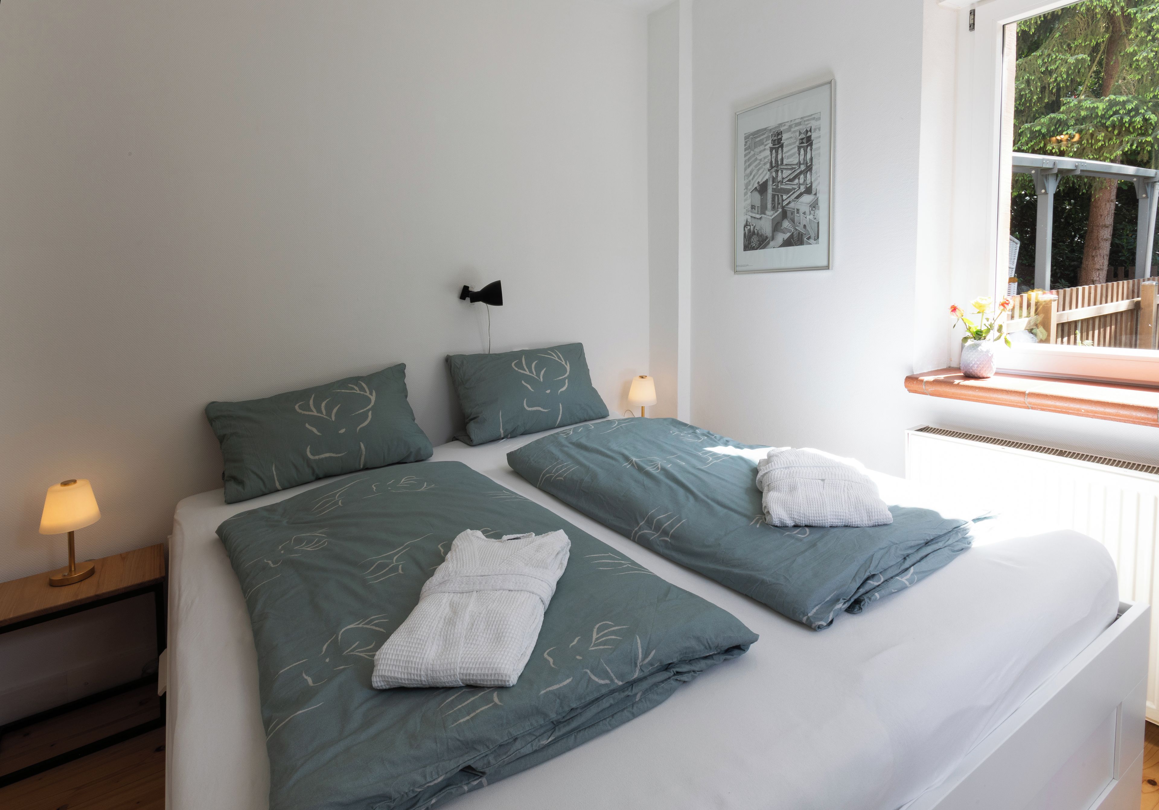 A double bed with two pillows, a bedside table with a lamp, and a window with a view of trees.