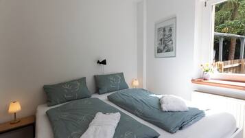 A double bed with two pillows, a bedside table with a lamp, and a window with a view of trees.