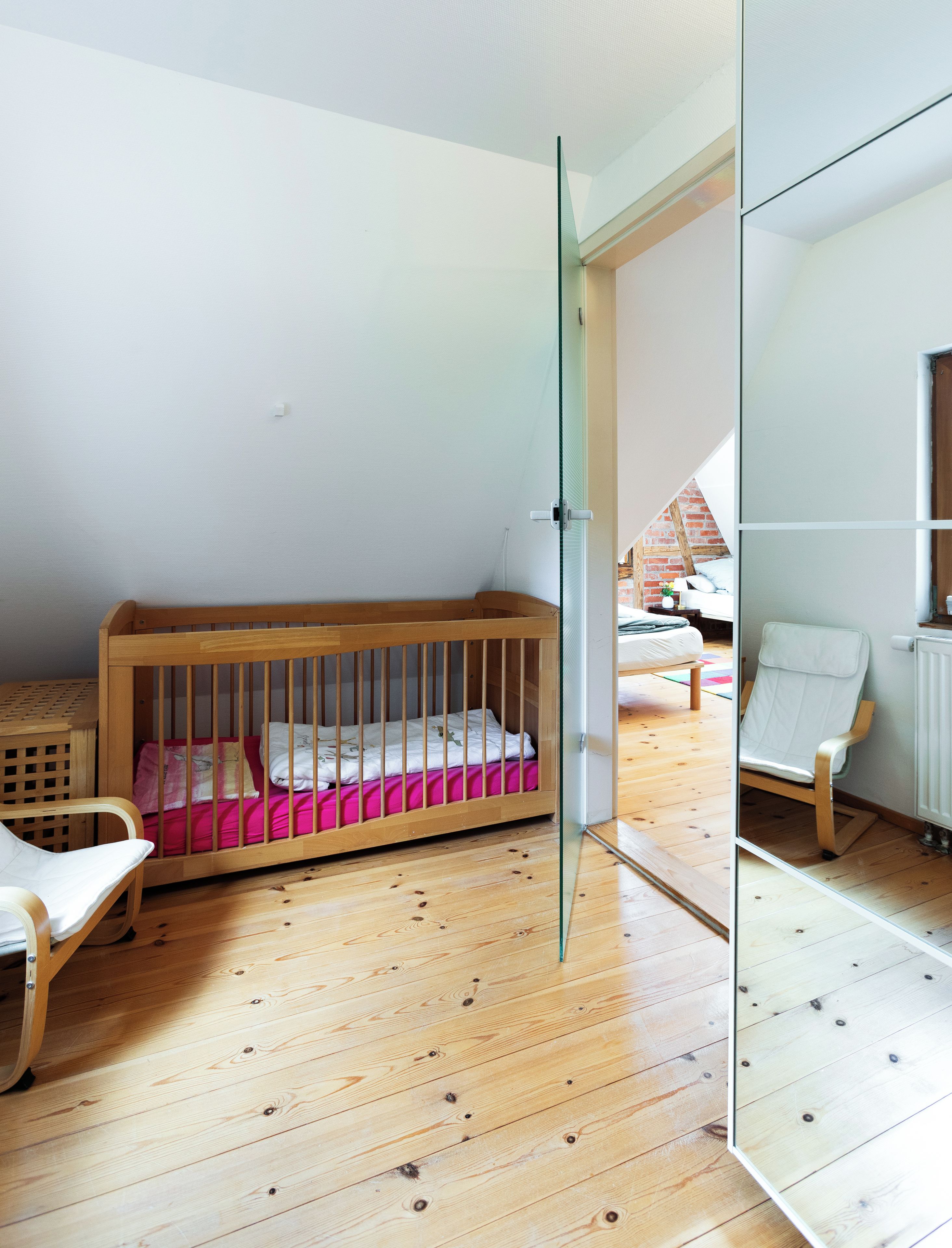 Une chambre d’enfant avec un berceau en bois, un fauteuil à bascule et une porte vitrée donnant sur une autre pièce.