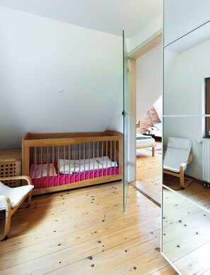Une chambre d’enfant avec un berceau en bois, un fauteuil à bascule et une porte vitrée donnant sur une autre pièce.