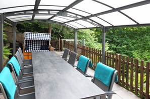 Eine Terrassenanlage im Freien mit überdachter Essgegend, Stühlen und einem Holzzaun.