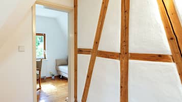 A room with a sloped ceiling, wooden beams, a white wall, and a wooden floor.