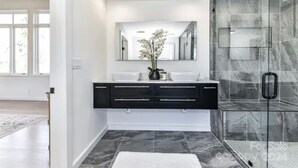 Un bany modern amb plat de dutxa de vidre, un lavabo negre i un mirall gran.