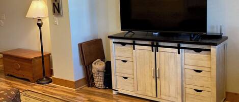 Una sala de estar con un televisor de pantalla plana sobre un mueble de madera, una lámpara, un sillón y un tapete con diseños de peces.
