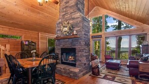 A cozy cabin interior with a stone fireplace, wooden dining table, and comfortable seating. - Mountain top cabin with big views, a relaxing hot tub and 2 gas fireplaces. (Ellijay)
