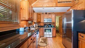 A wooden cabin-style kitchen with a large refrigerator, stove, and microwave. - Mountain top cabin with big views, a relaxing hot tub and 2 gas fireplaces. (Ellijay)