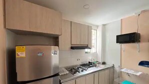 A compact kitchen with light wood cabinets, a stainless steel refrigerator, a microwave, and a gas stove.