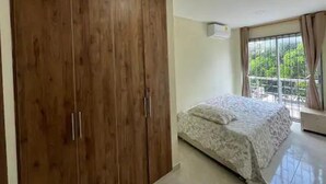 A bedroom with a large wooden wardrobe, a bed with a patterned bedspread, and a window with curtains.