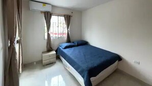 A bedroom with a bed, a nightstand, a window with curtains, and an air conditioning unit.