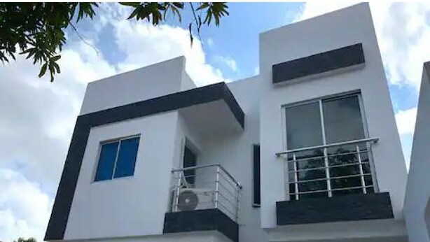 A modern two-story building with a balcony on the upper floor, large windows, and a visible air conditioning unit.