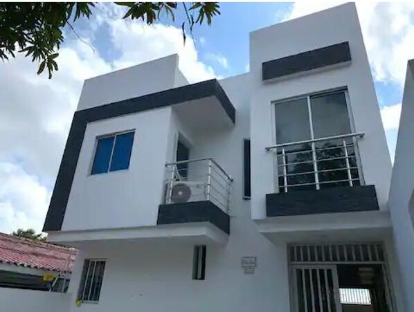 Two-story building with a flat roof and minimalist design, featuring a balcony and entrance with a door and window.