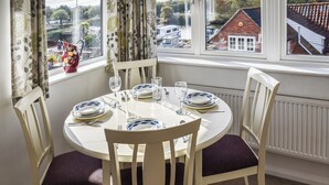 A dining table set for four with white chairs and purple cushions, positioned by a window with a view of boats and houses. - A perfect waterside setting. (Horning)