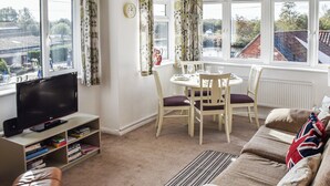A living room with a television, a sofa, a dining table with chairs, and a view of a river and buildings through large windows. - A perfect waterside setting. (Horning)