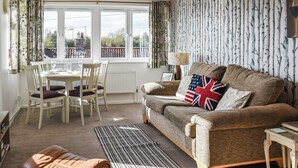 A cozy living room with a sofa, a dining table with chairs, a coffee table, and a view through large windows. - A perfect waterside setting. (Horning)