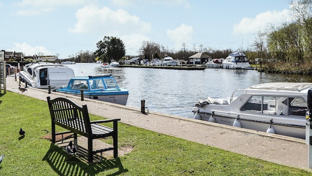 A riverside view with boats docked, a bench, and a grassy area. - A perfect waterside setting. (Horning)