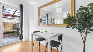 A dining area with a white table, black chairs, a large mirror, and a potted plant. - Cozylease 3-Bed Retreat Near O2/LCY with Gym, Workspace, Garden & Free Parking (London)