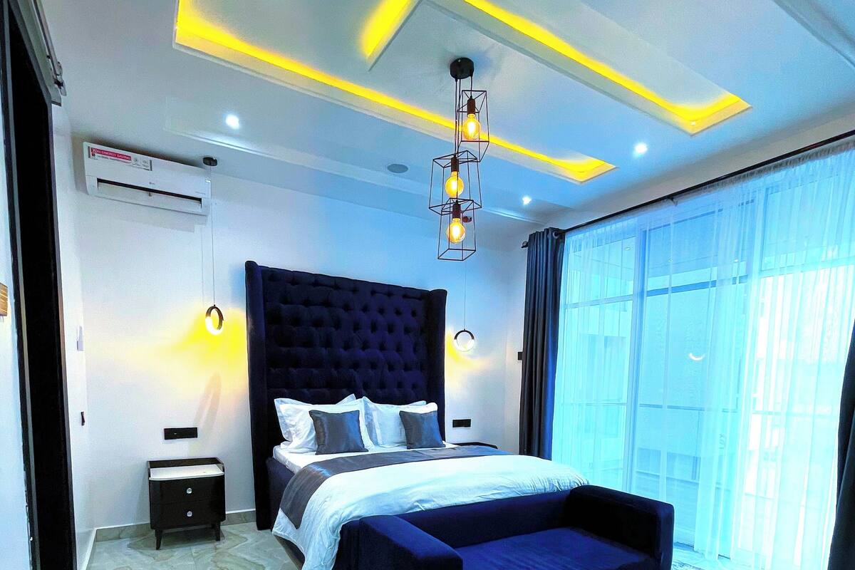 A modern bedroom with a large bed, a bedside table, a nightstand, and a floor lamp.