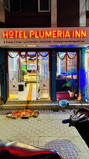 Hotelli Plumeria Innin ulkopuoli, jossa on kyltti, yhteystiedot ja moottoripyörä pysäköitynä sen eteen.