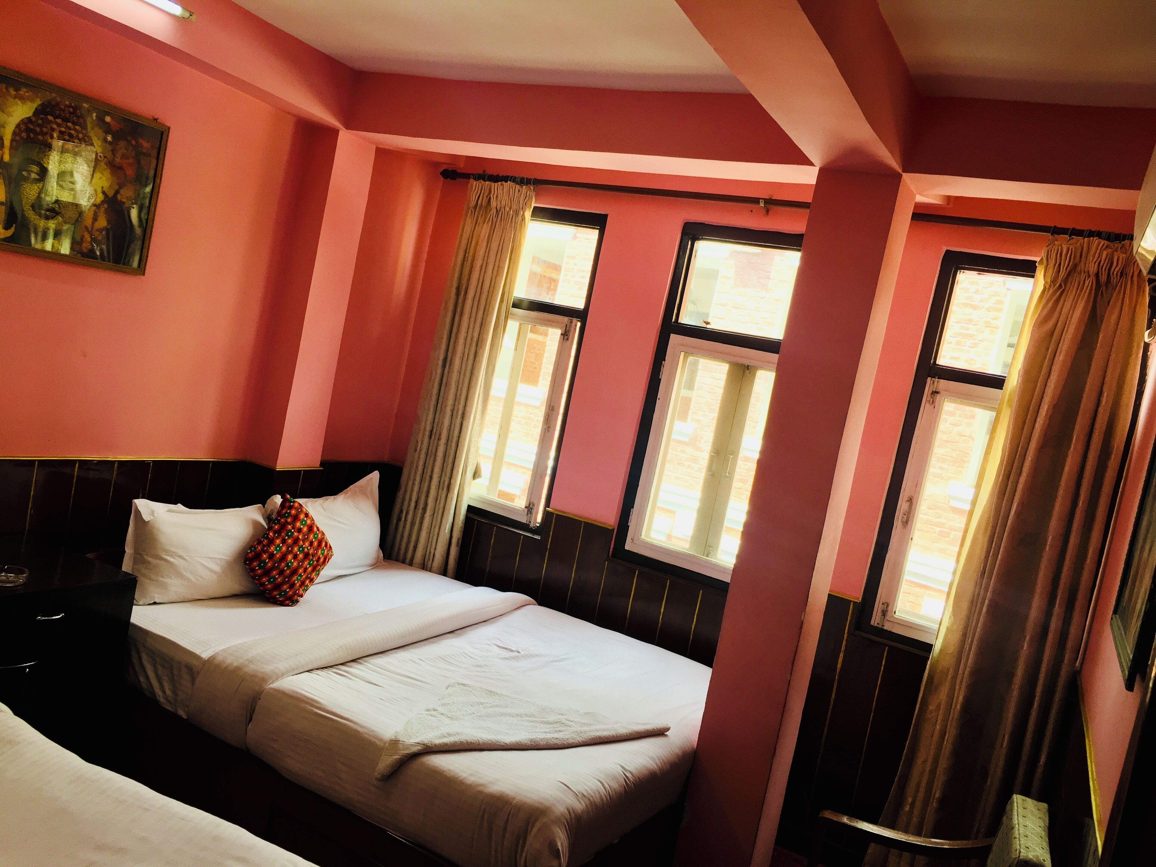 A room with pink walls, two beds, a headboard, and a window with curtains.