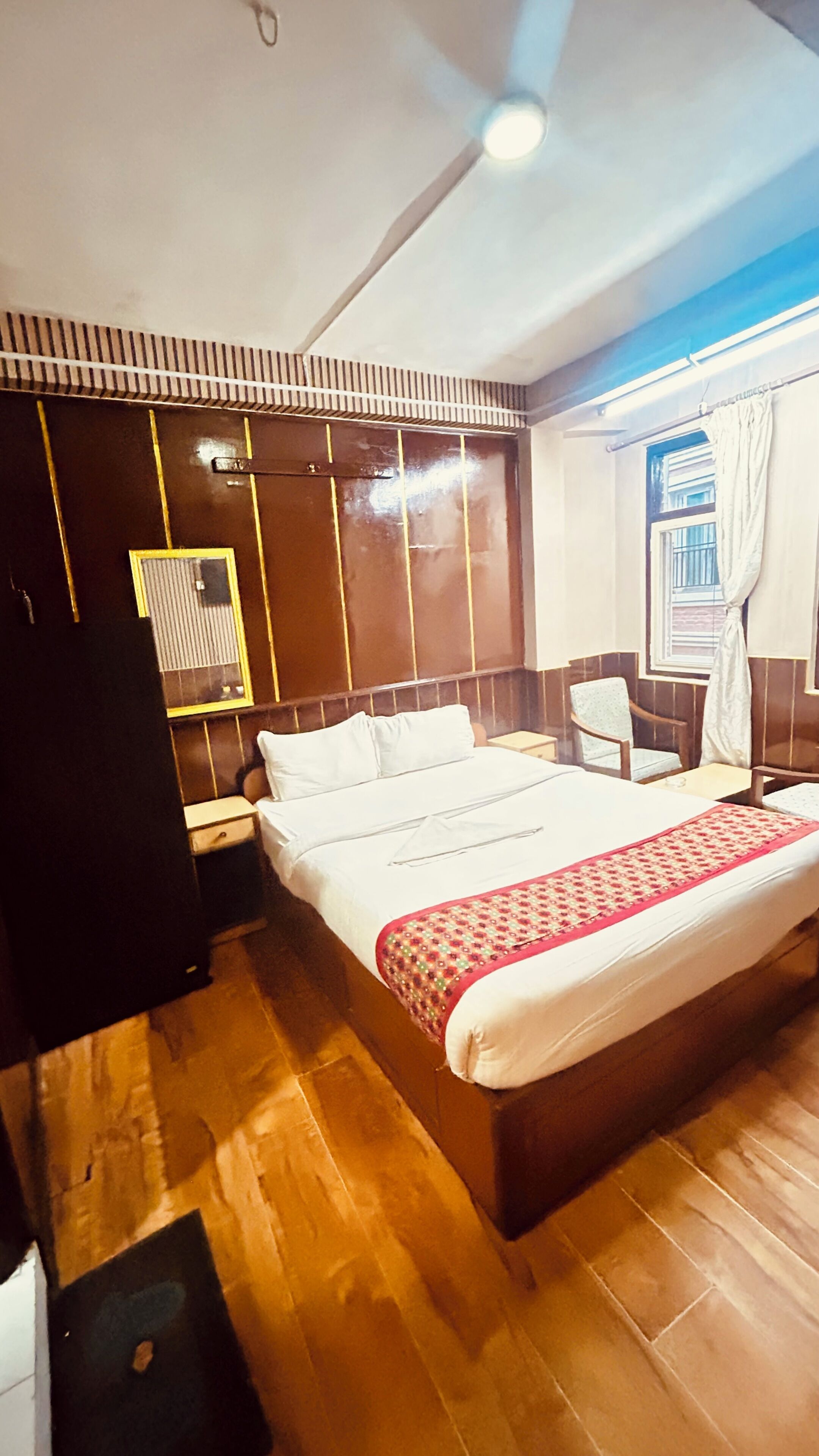 Een hotelkamer met een groot bed, een nachtkastje, een stoel, een kledingkast en een raam met gordijnen.