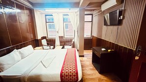 Habitación de hotel con una cama grande, un escritorio, una silla, un televisor y ventanas con cortinas.
