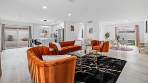 En rummelig stue med et moderne orange sofasæt, et glastæppe og en sort måtte med guldlinjer.