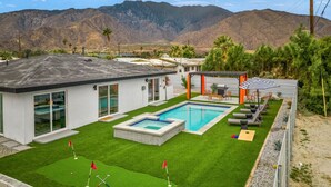 Et moderne hus med swimmingpool, tennisbane og en patio med udendørs møbler.