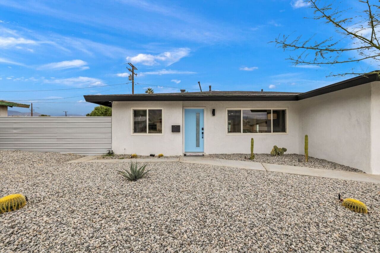 A single-story building with a light blue door, a small porch area, and a gravel driveway.