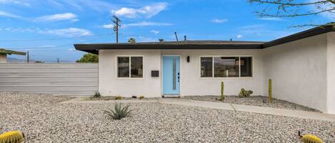 A single-story building with a light blue door, a small porch area, and a gravel driveway.