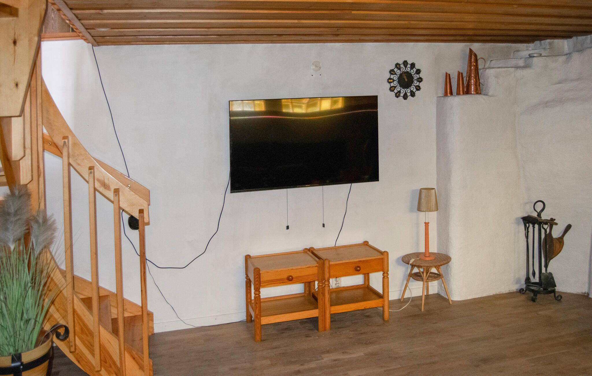 A room with a wooden bench, a small table, a wall-mounted TV, and a decorative clock.